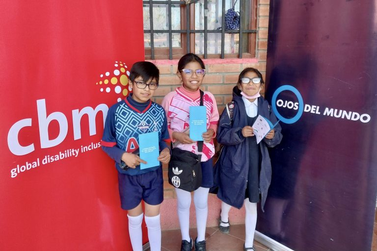 Dos niñas y un niño con gafas delante de expositor de CBM y Ojos del mundo